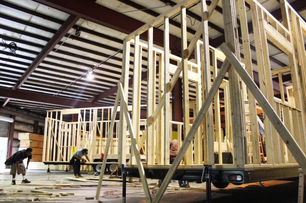 Tiny Home Builders Working Indoors on Trailer Frame Structure Tiny home builders constructing a trailer-based tiny house inside a workshop facility