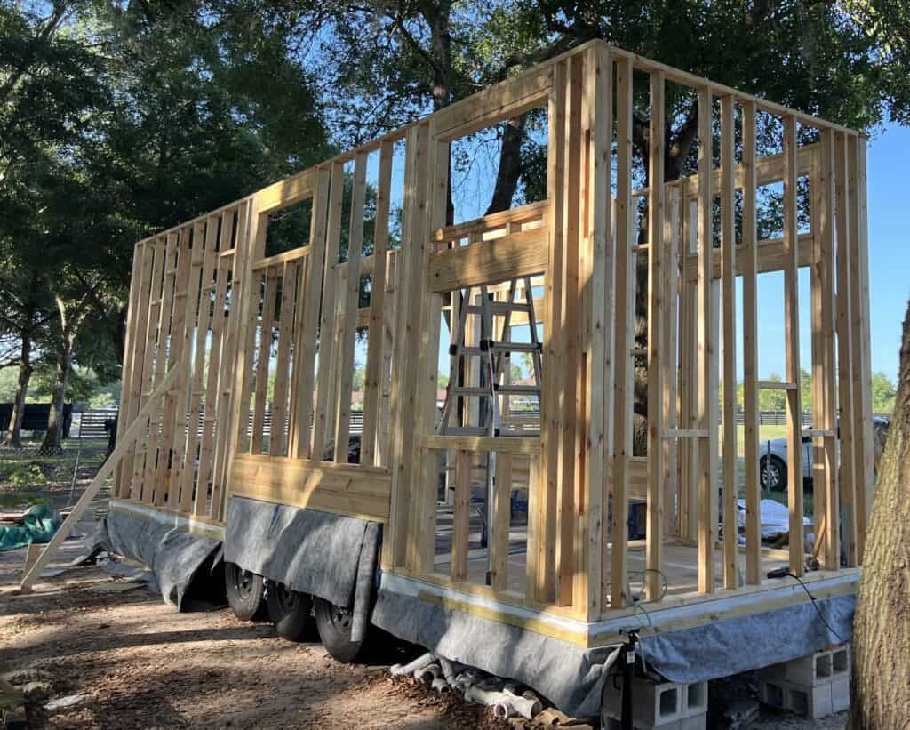 Tiny home builders assembling the wooden frame of a mobile tiny house under trees