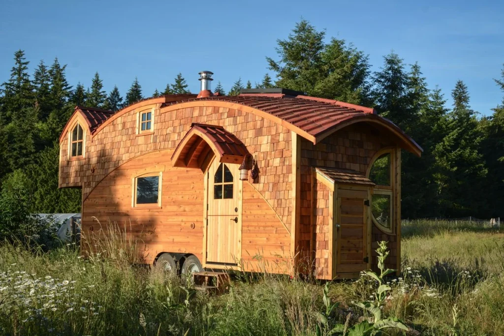Shingled Tiny Home with Curved Roof Design Curved roof tiny home with shingle siding set in a lush green field by a top tiny home builder.