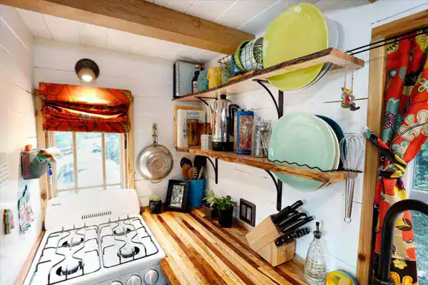 Tiny home kitchen with wooden shelves and hanging utensils, part of tiny home kitchen storage ideas.