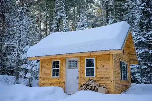 Wooden cabin in snow illustrating how to heat a tiny home in winter using wood stoves and insulation